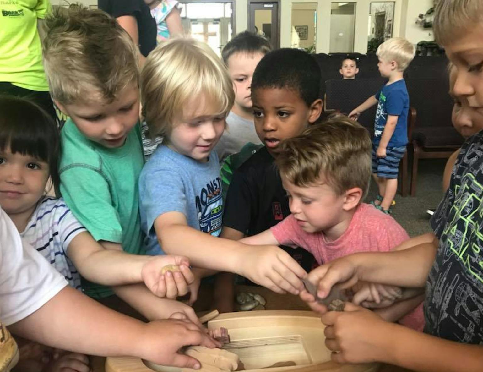 Group of children gathered around a wooden bowl, reaching in