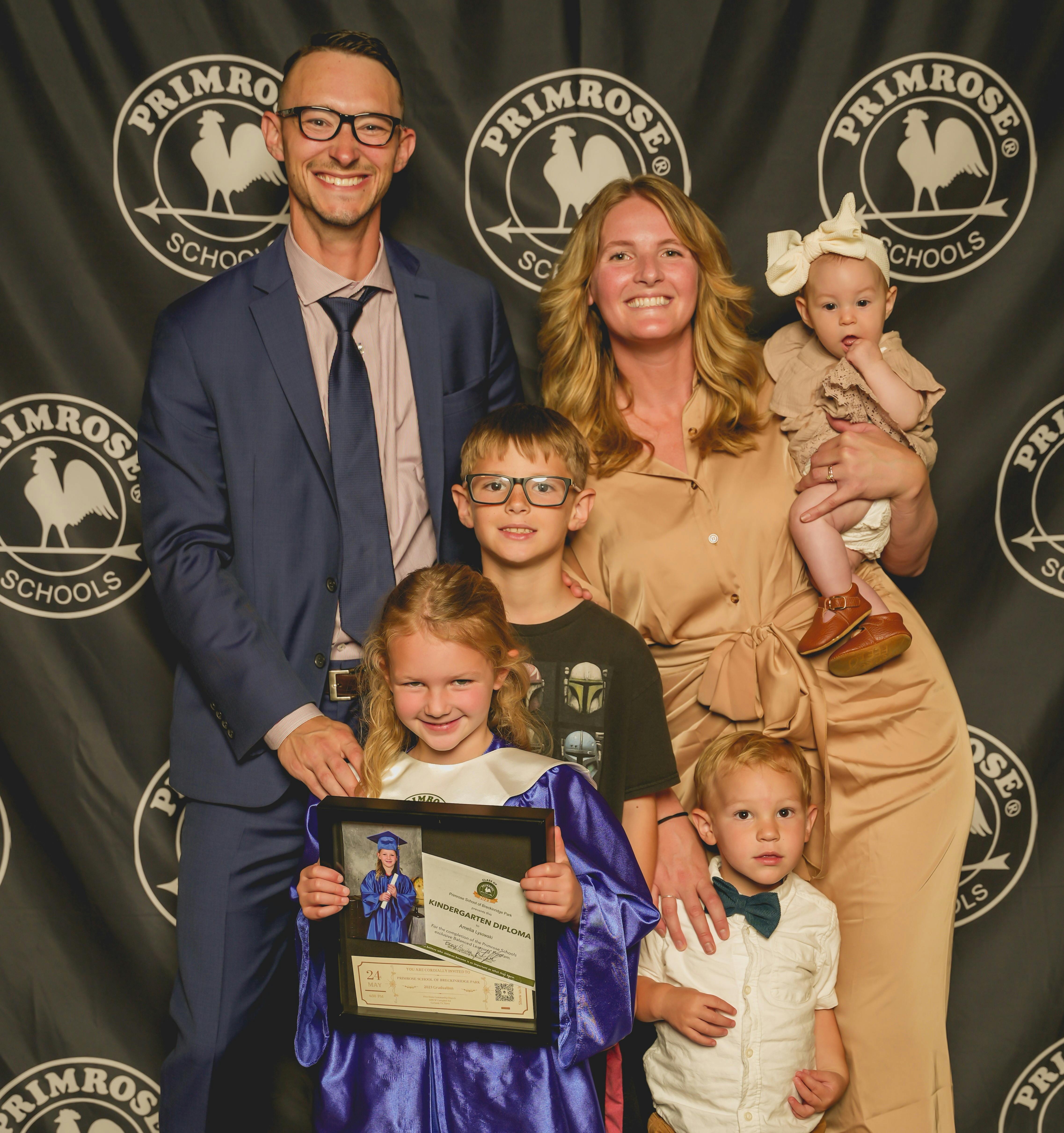 Family posing in front of a school backdrop with a child holding a diploma