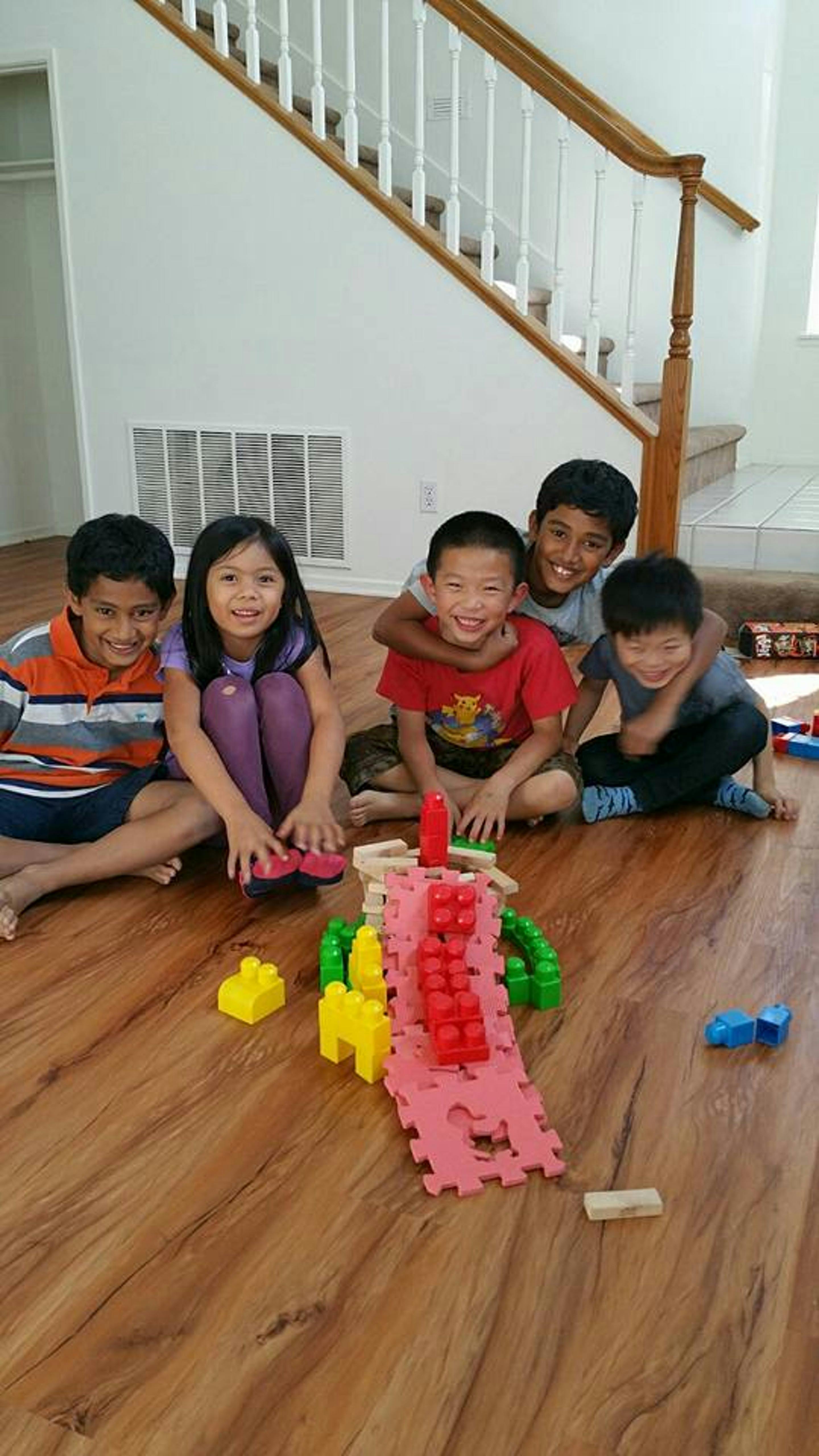 Five children sitting on a wooden floor with building blocks