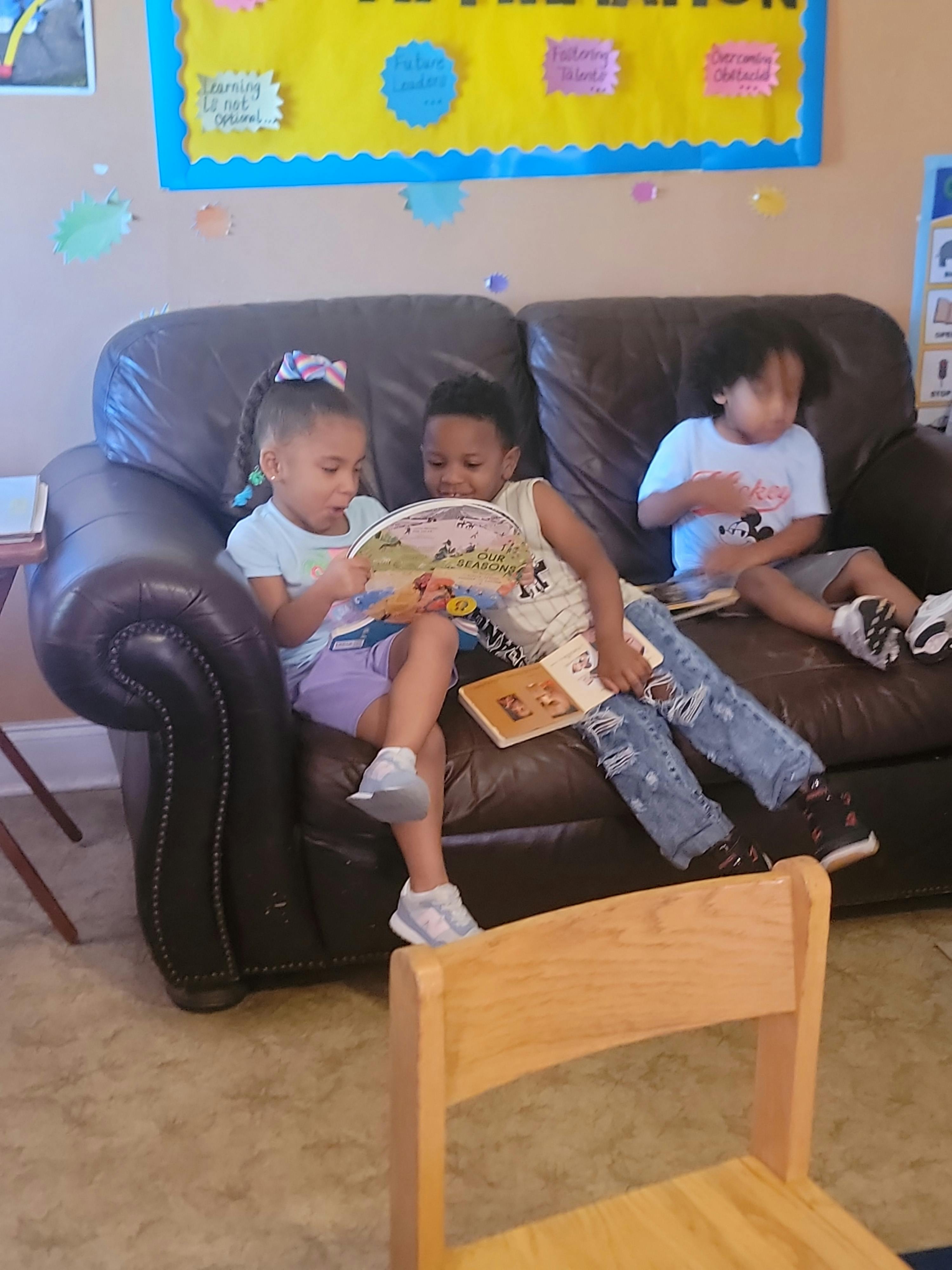 Three children sitting on a couch, two reading a book together