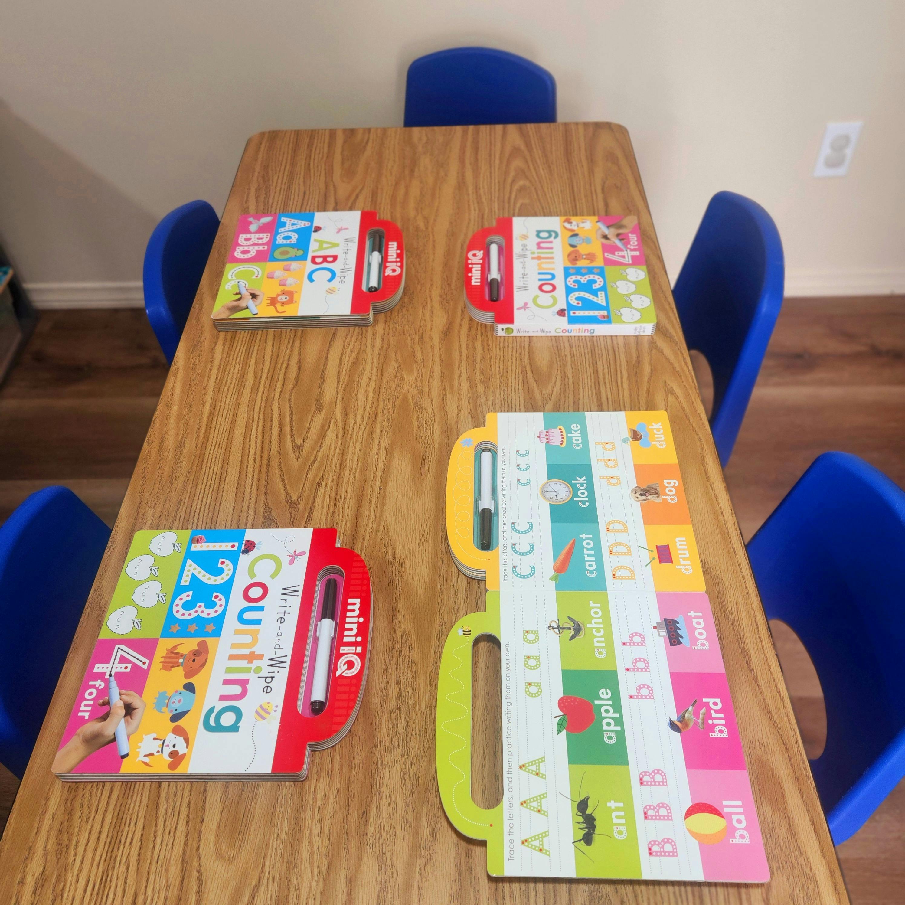 Children's learning books on a wooden table with blue chairs