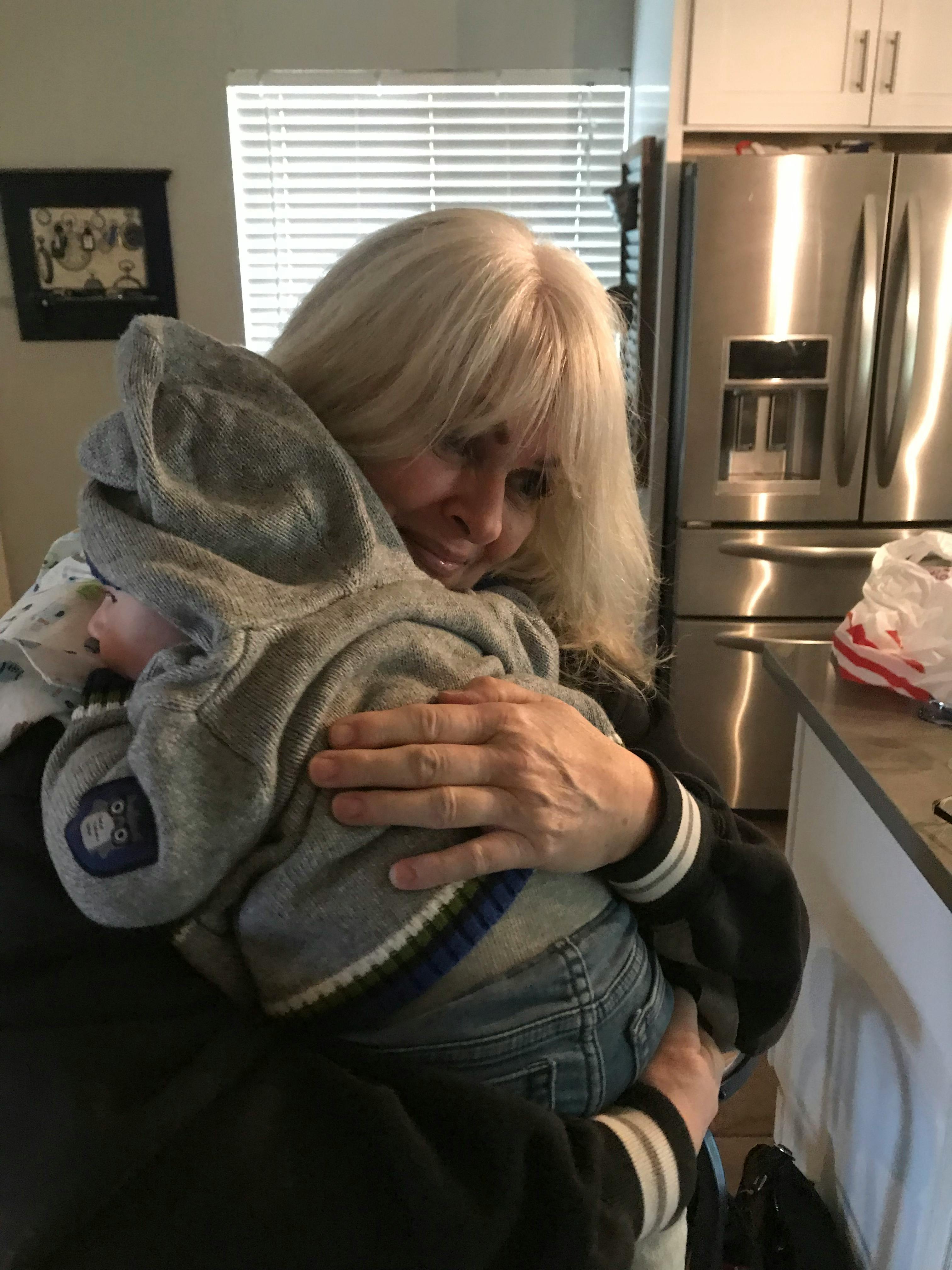 Person holding a child in a gray hooded outfit
