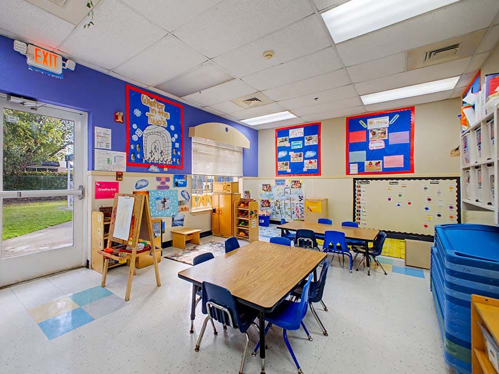 Classroom with child-sized tables and chairs, bulletin boards, and an easel