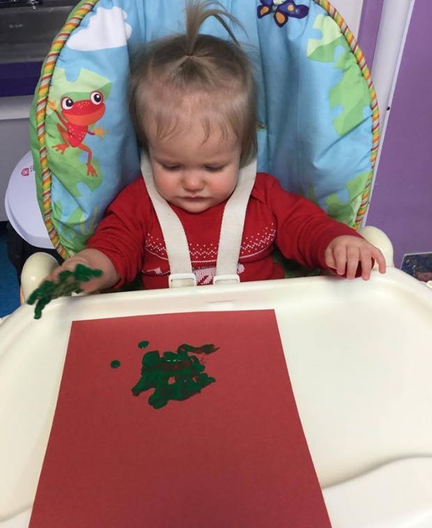 Child in high chair finger painting with green paint on red paper