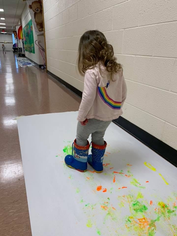 Child in boots standing on paper with paint splattered paint