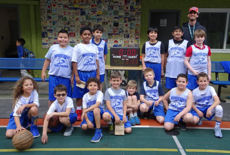 Children's basketball team posing with an adult and scoreboard
