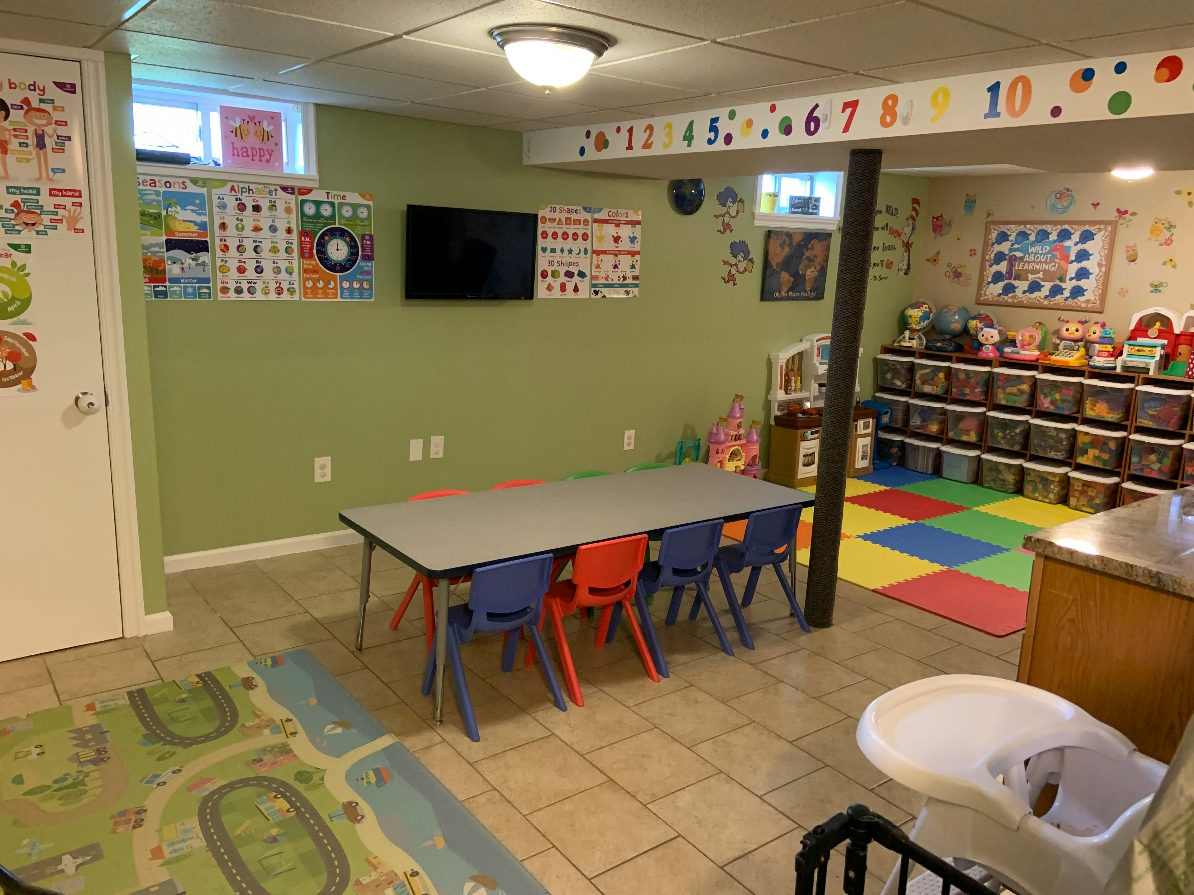 Playroom with a long table and colorful chairs, storage shelves, and a play mat
