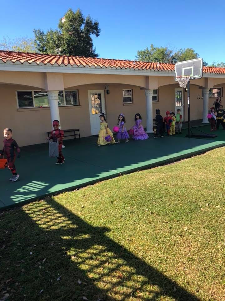 Children in costumes walking on a green surface outside a building