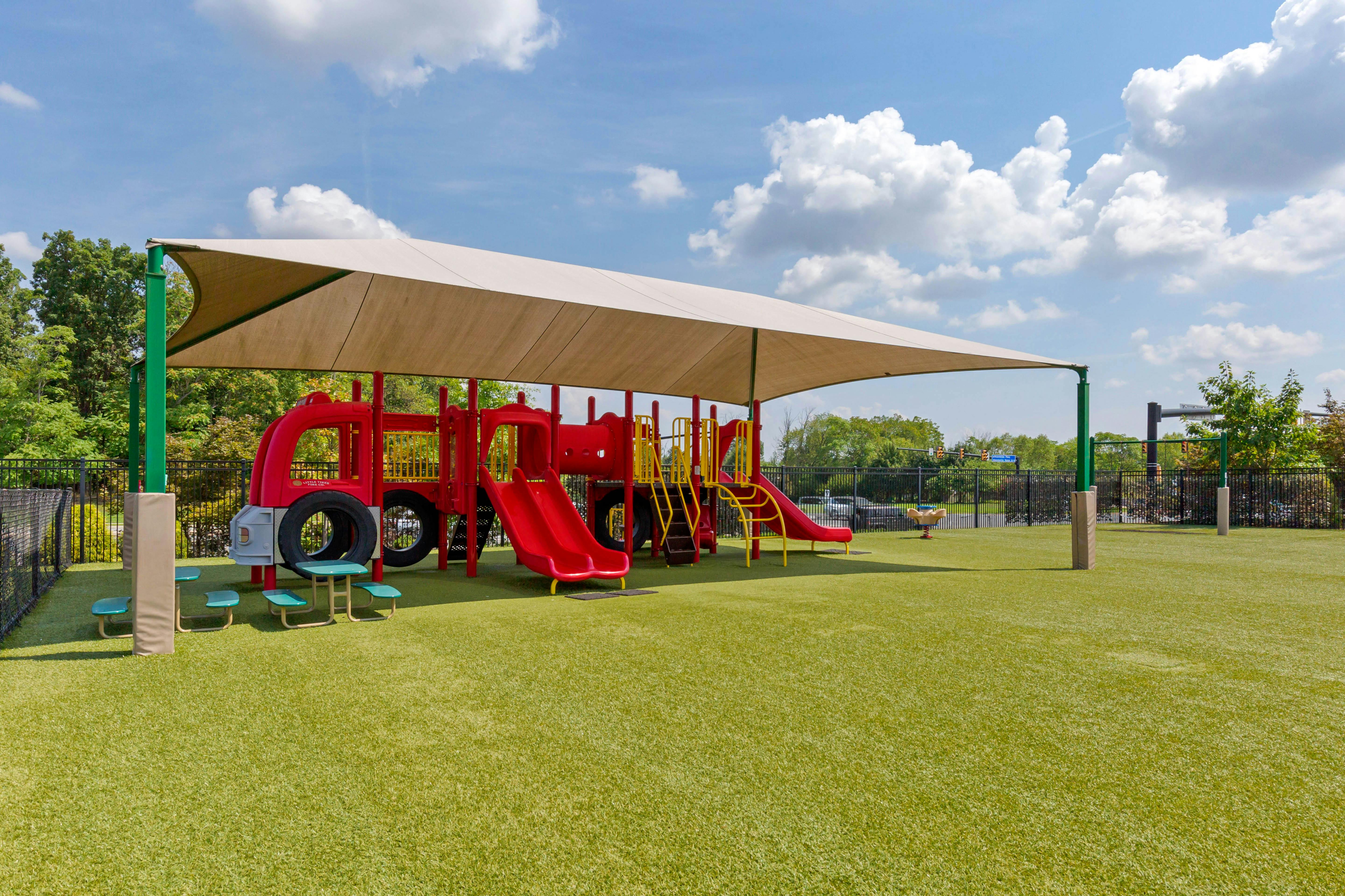 Playground with red fire truck structure and slides under a shade canopy