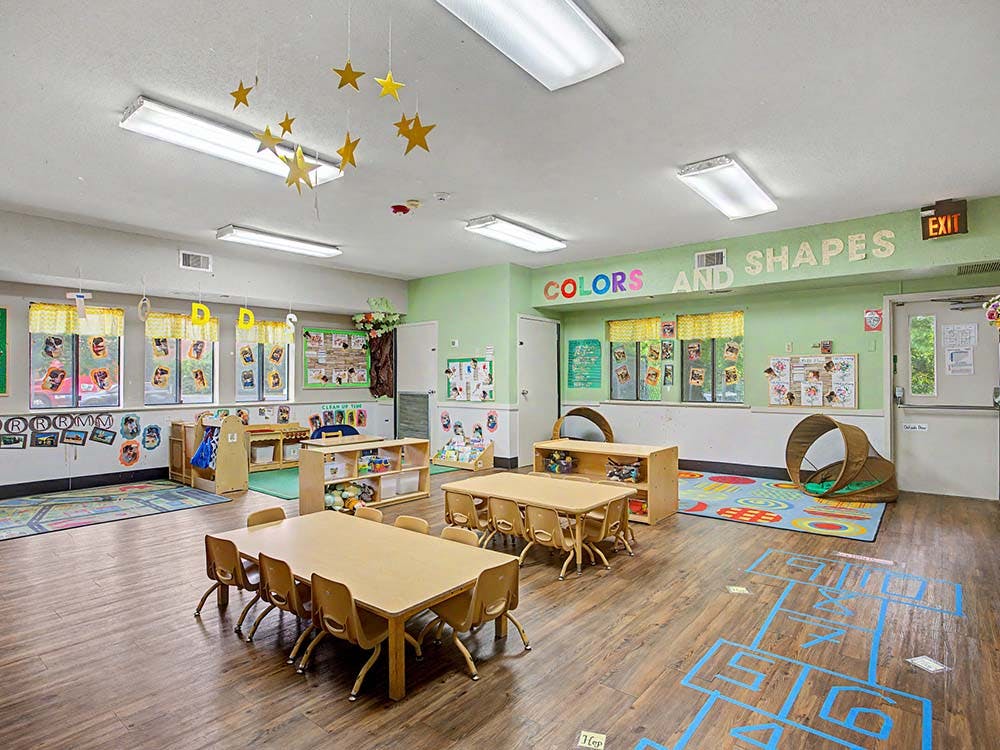 Empty classroom with small tables and chairs, colorful rugs, and decorations