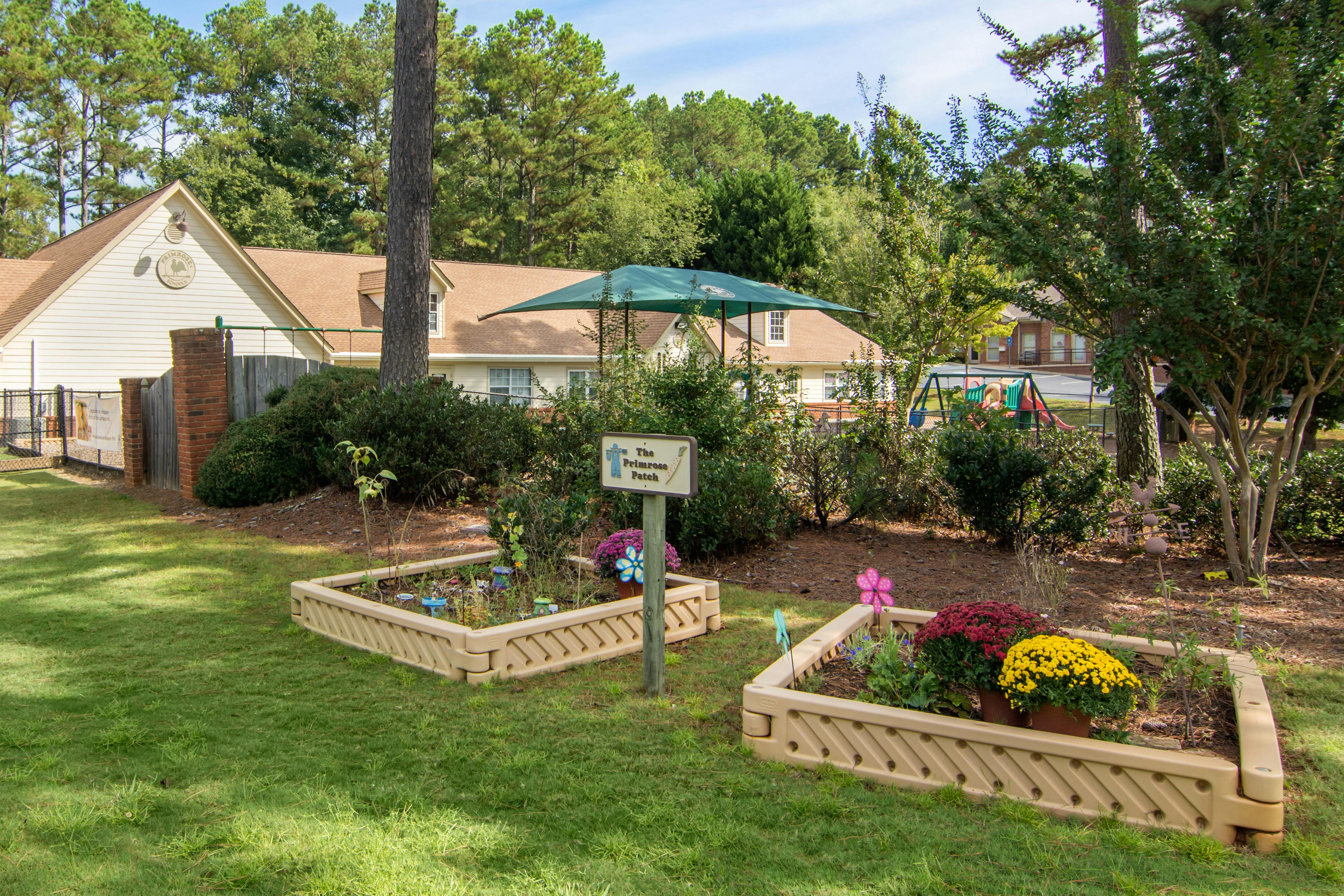 Raised garden beds with plants and flowers, Primrose Patch sign, playground in background