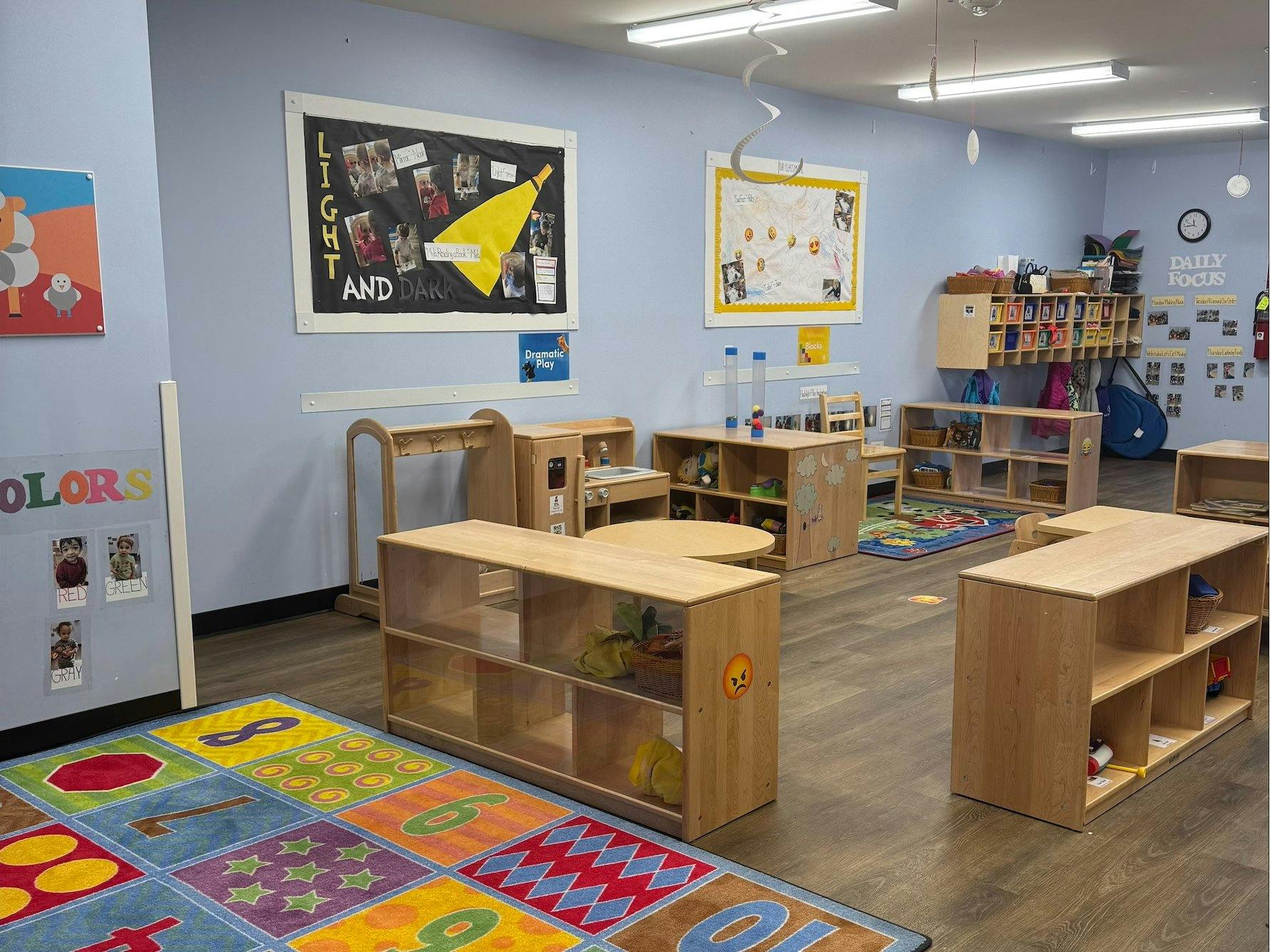 An empty early childhood classroom with low shelves, tables, and a colorful rug
