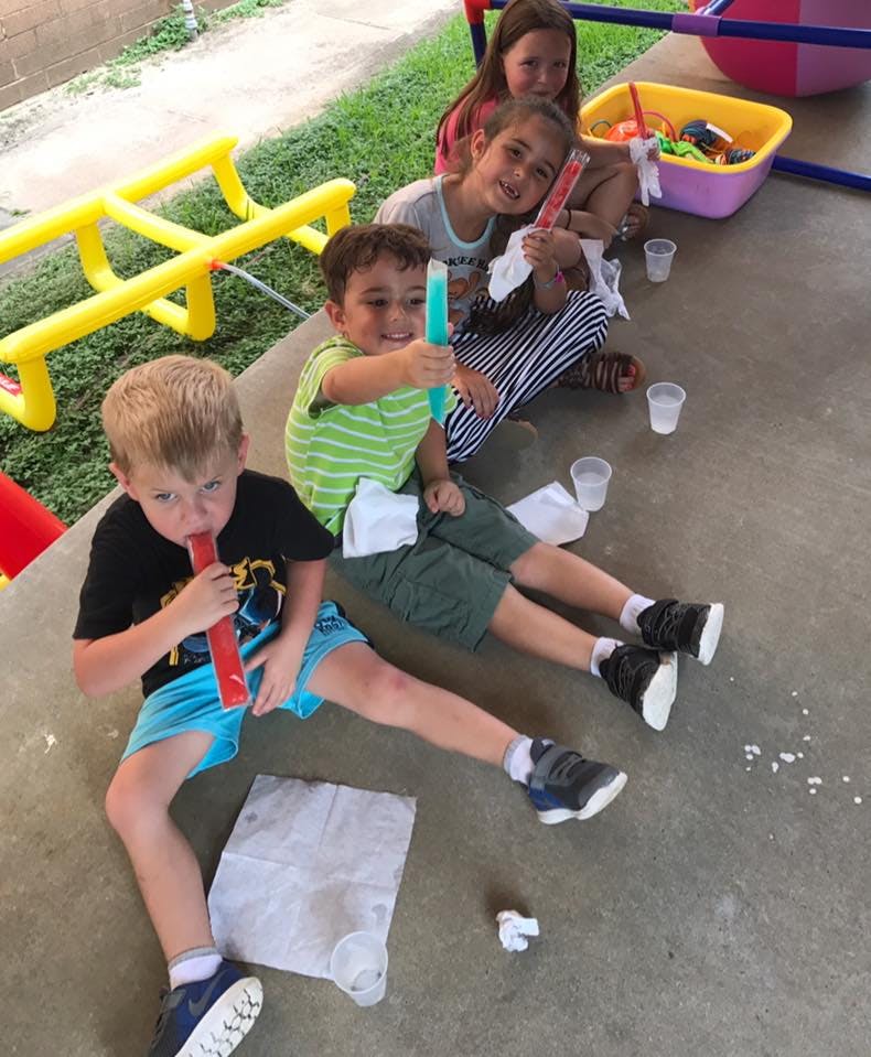 Four children sitting on the ground eating popsicles