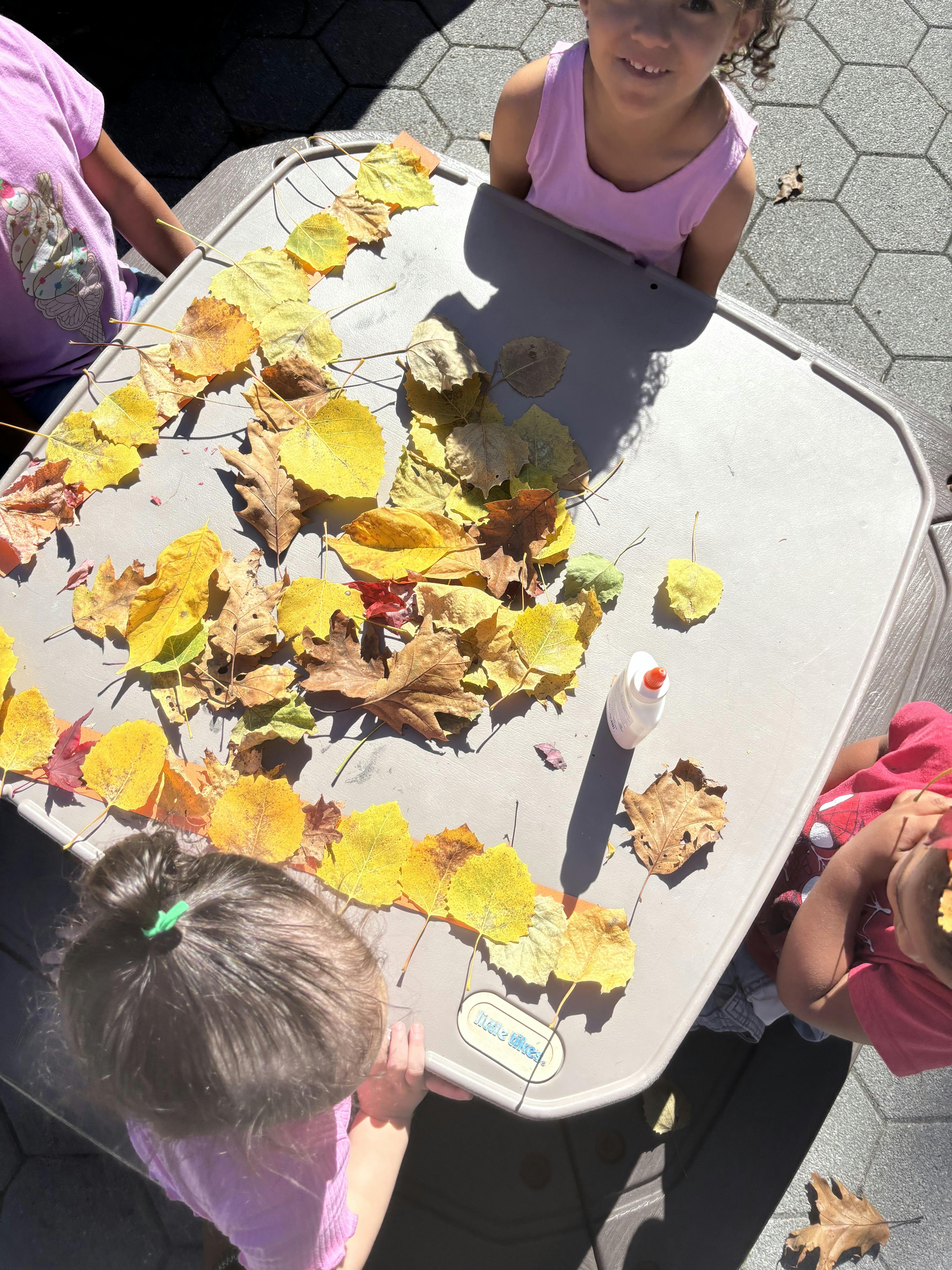 Children making art with autumn leaves and glue on a table