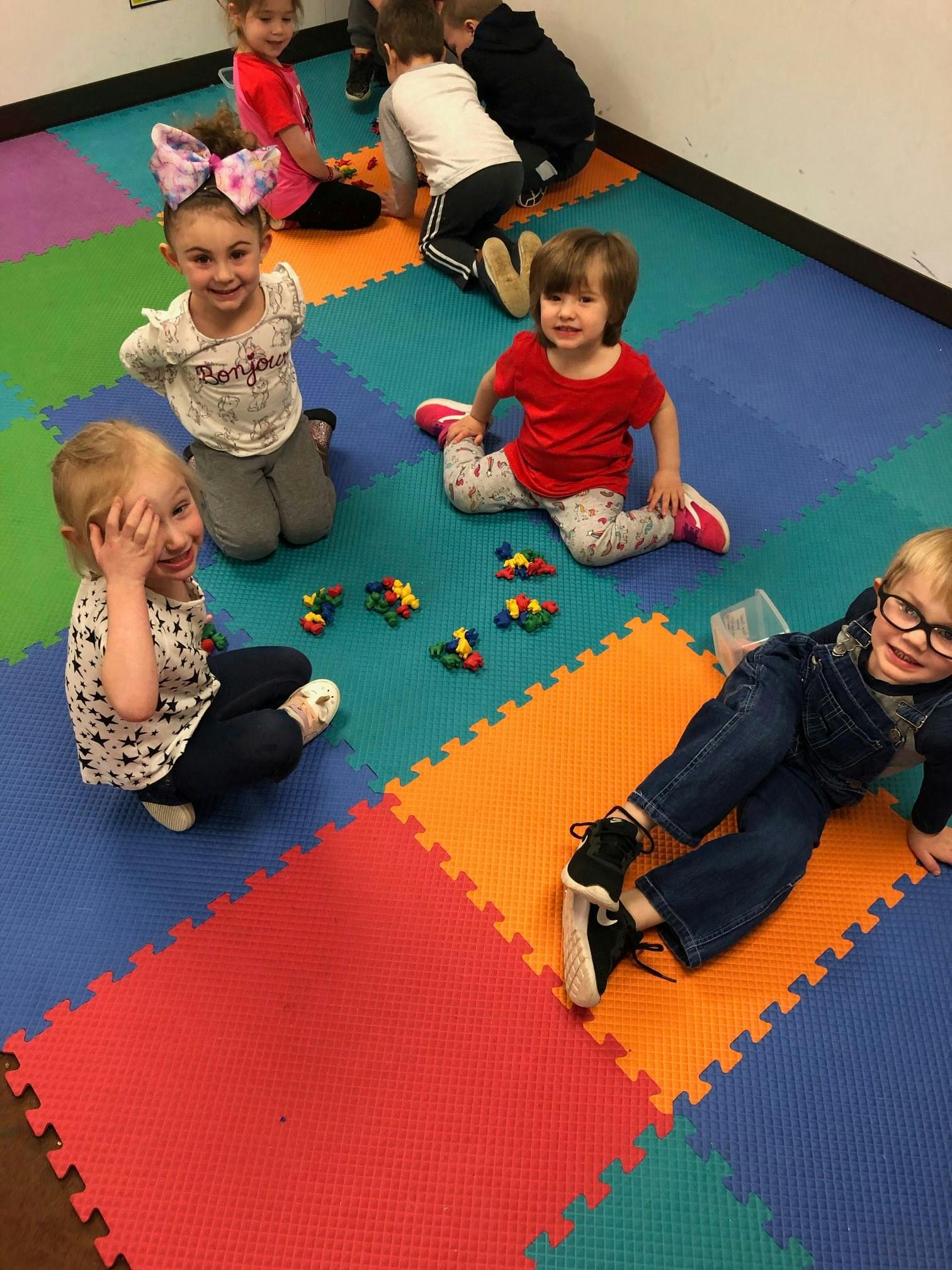 Children playing on a colorful mat with small toys
