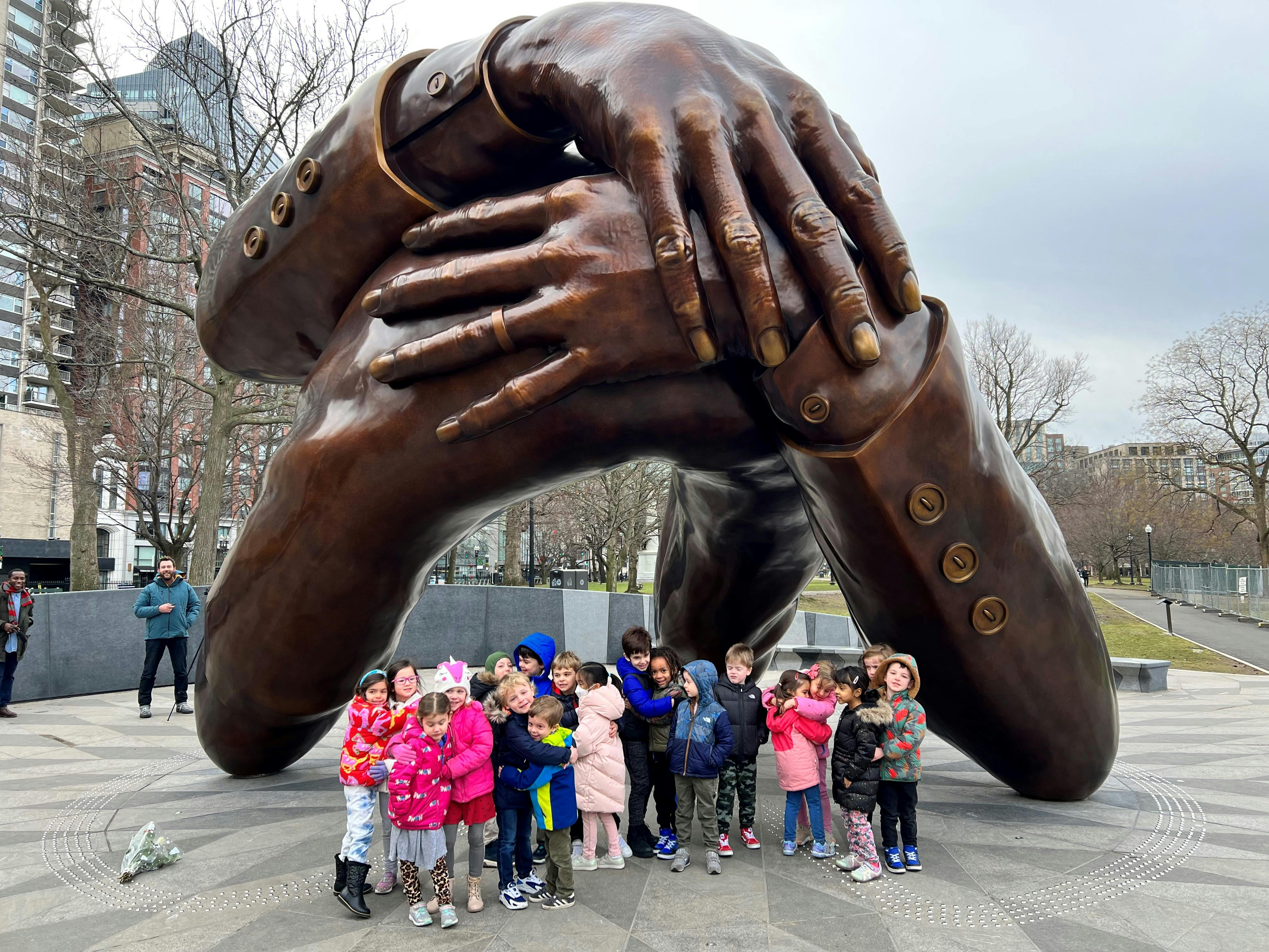 Children standing in front of a large bronze sculpture of intertwined arms