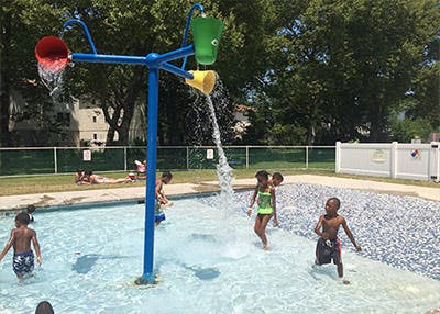 Children playing in a splash pad with water buckets