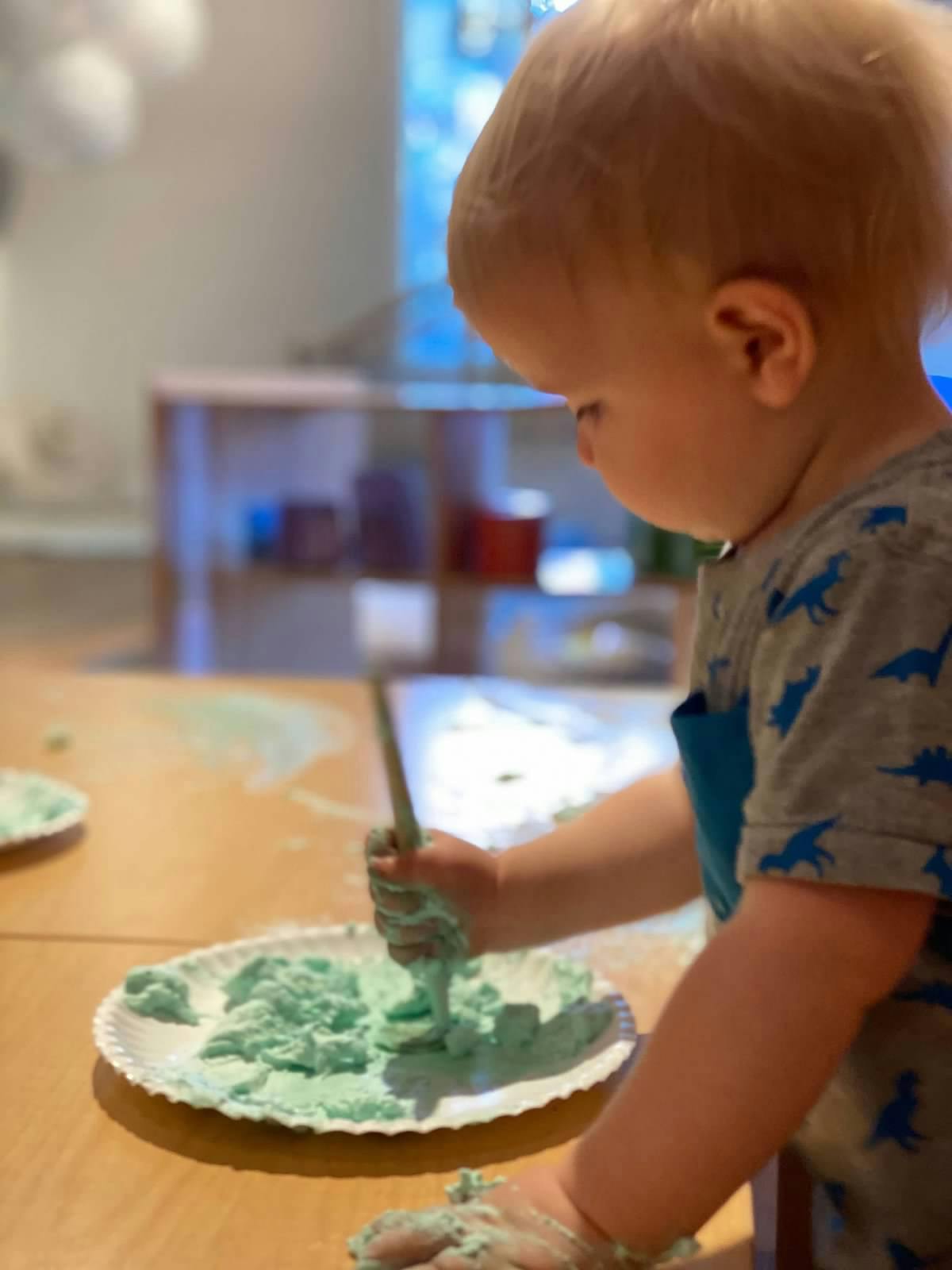 Child playing with green dough on a paper plate
