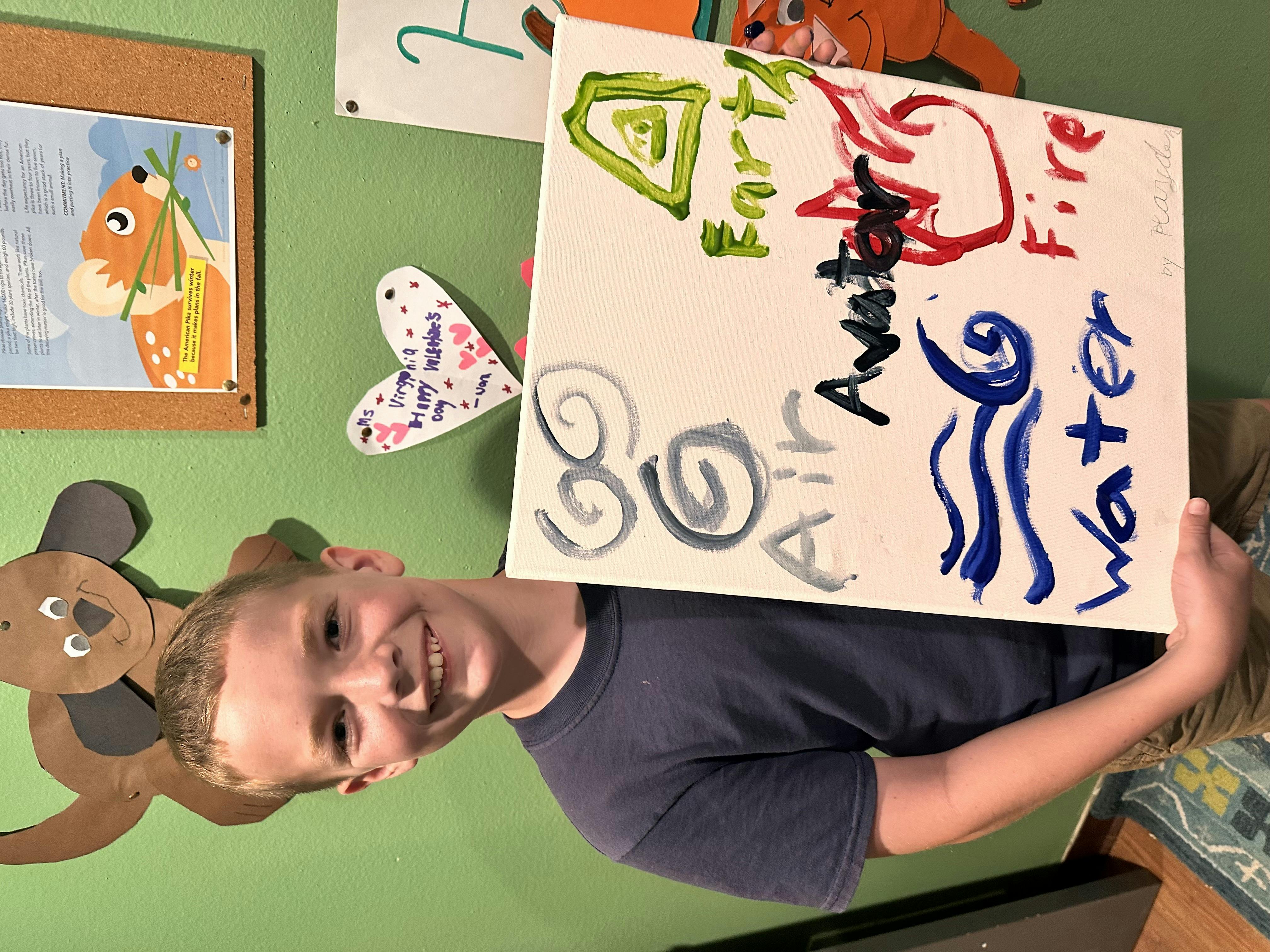 Child holding a painting with "Earth, Fire, Air, Water, Avatar" written on it