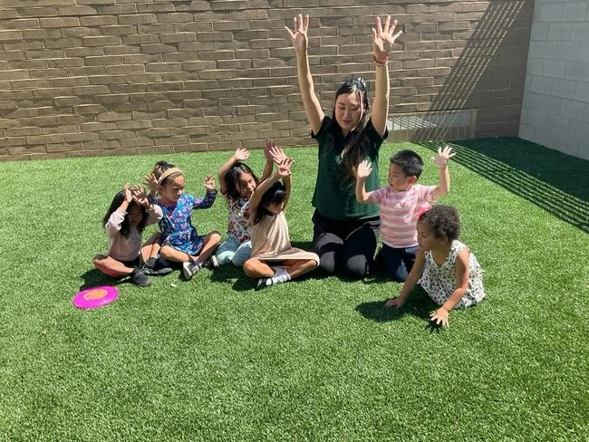 Group of children and a person sitting on grass with hands raised
