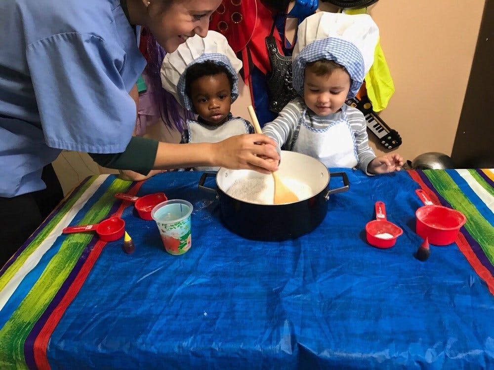 Adult and two children in chef hats mixing ingredients in a pot
