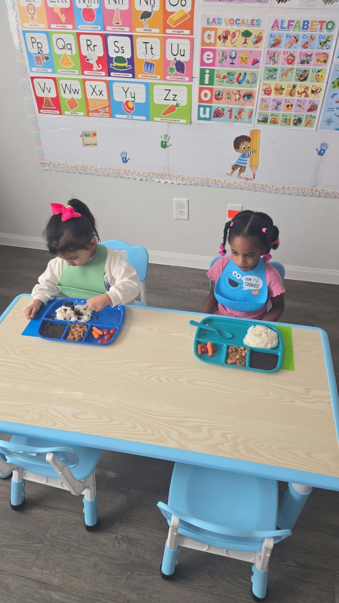Two children sitting at a table with divided plates of food