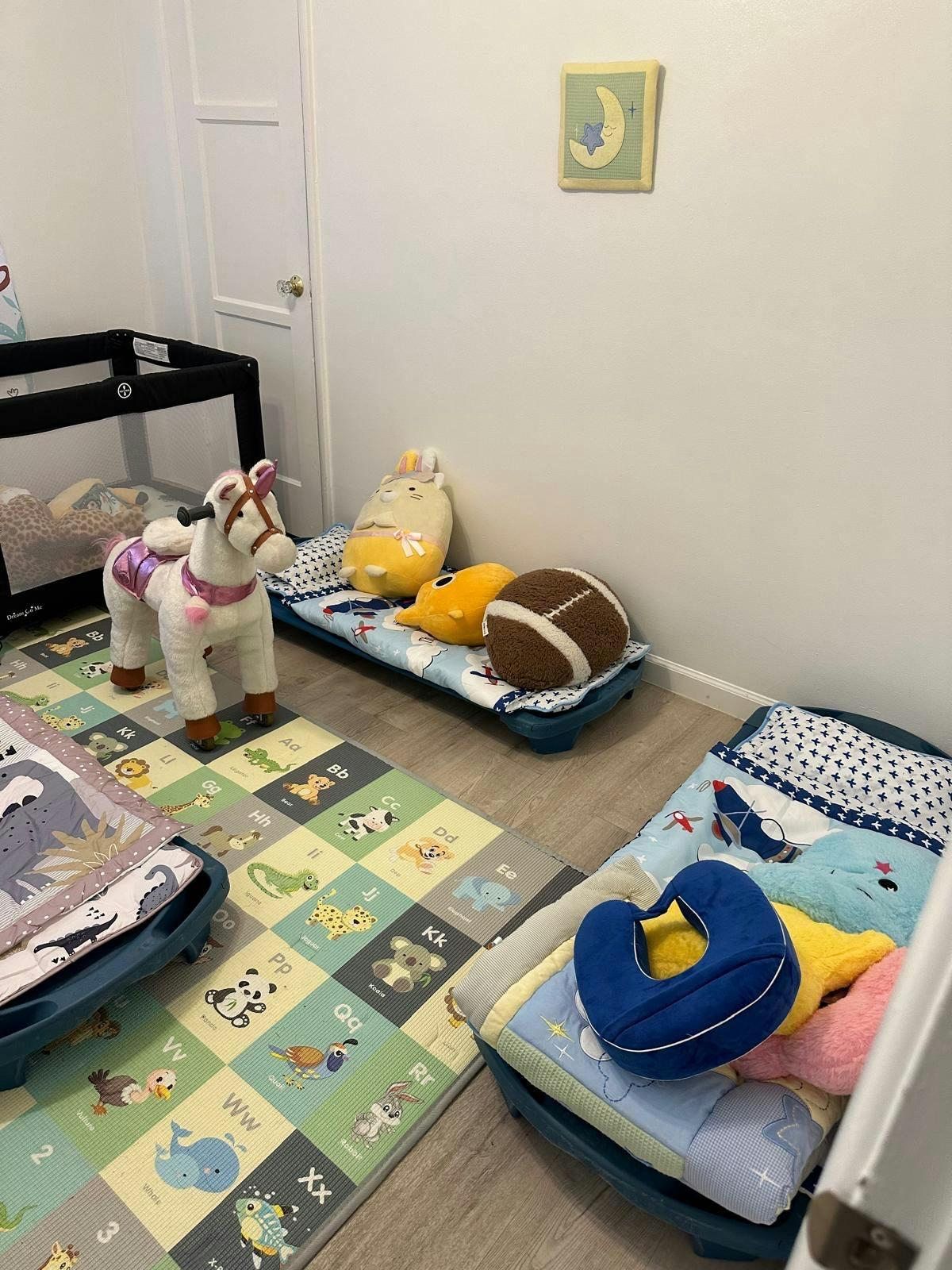 Toddler room with cots, play mat, and rocking horse