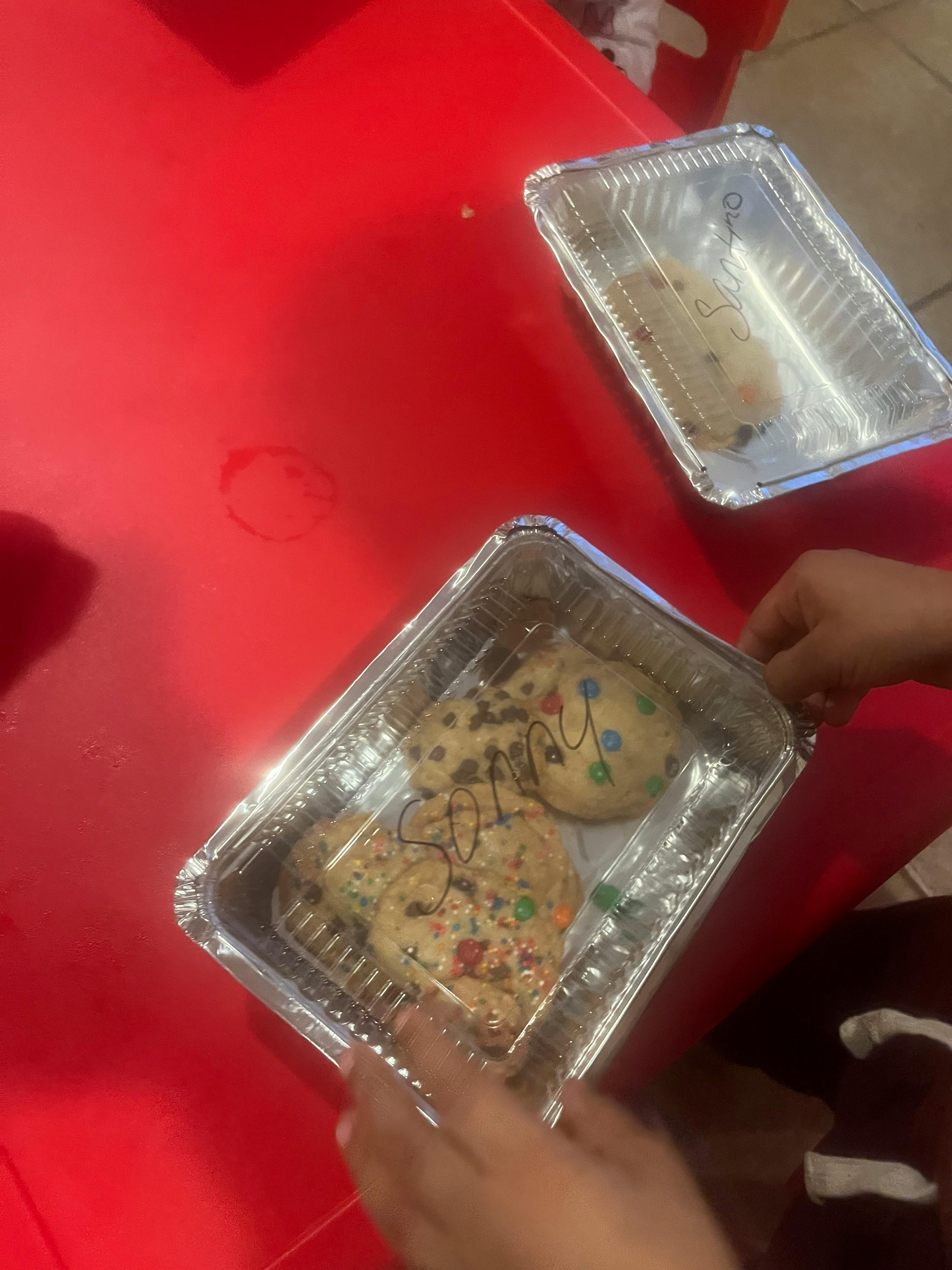 Person's hands holding a foil container with cookies on a red surface