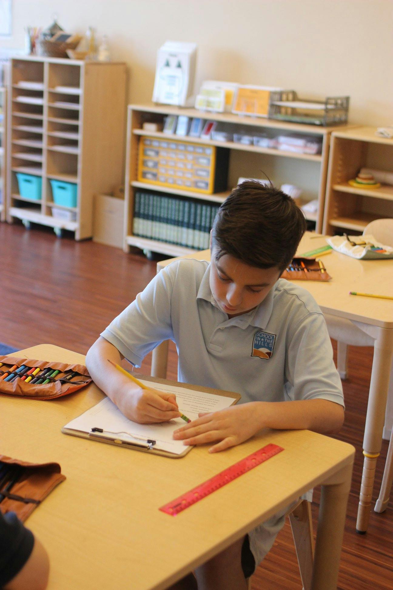 Child writing on paper at a desk in a classroom