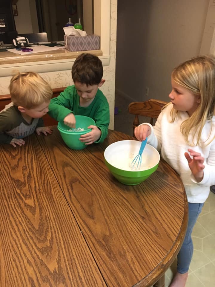 Three children mixing ingredients in bowls on a wooden table