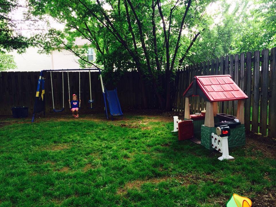 Child on a swing set in a backyard with a playhouse