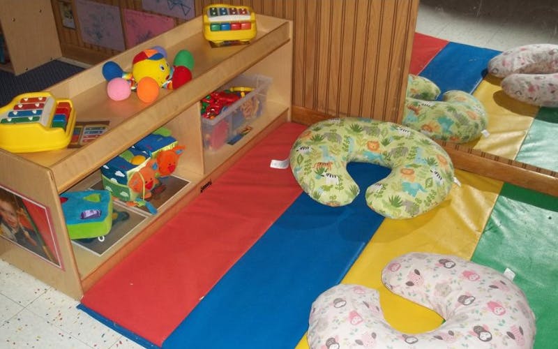 Children's play area with toys on shelves, activity mat, and nursing pillows