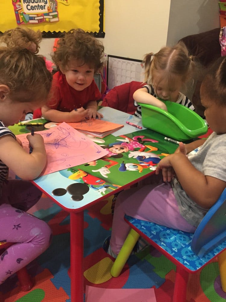 Children sitting at a table, drawing and playing with toys