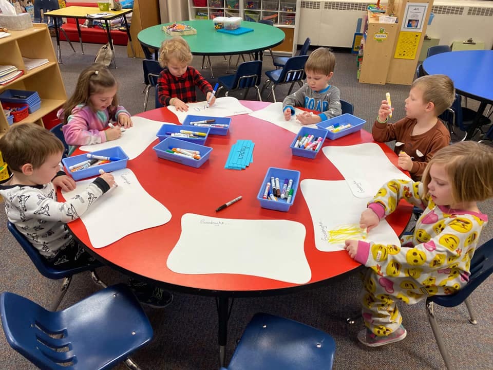 Children drawing at a red table in a classroom