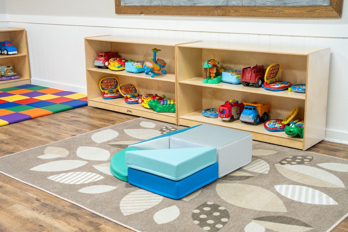 Wooden toy shelves filled with various plastic toys and foam blocks on a rug