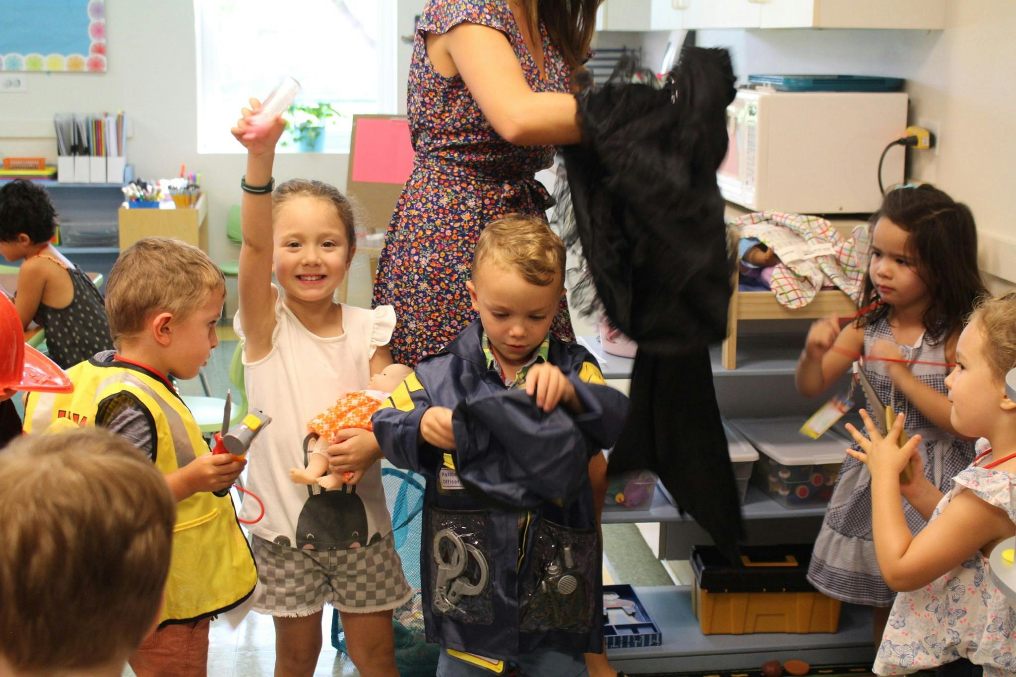 Adult helping children with dress-up clothes in a classroom