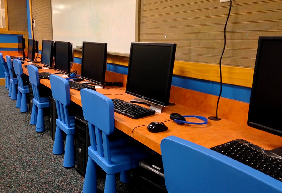 Row of computers with keyboards, mice, and headphones on orange desks with blue chairs