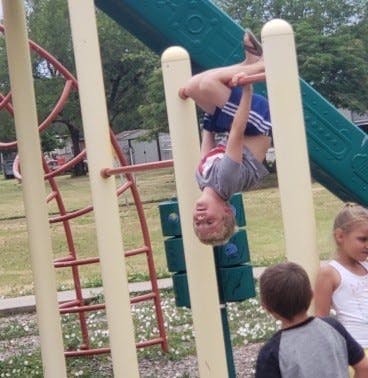 Child hanging upside down from a bar on a playground
