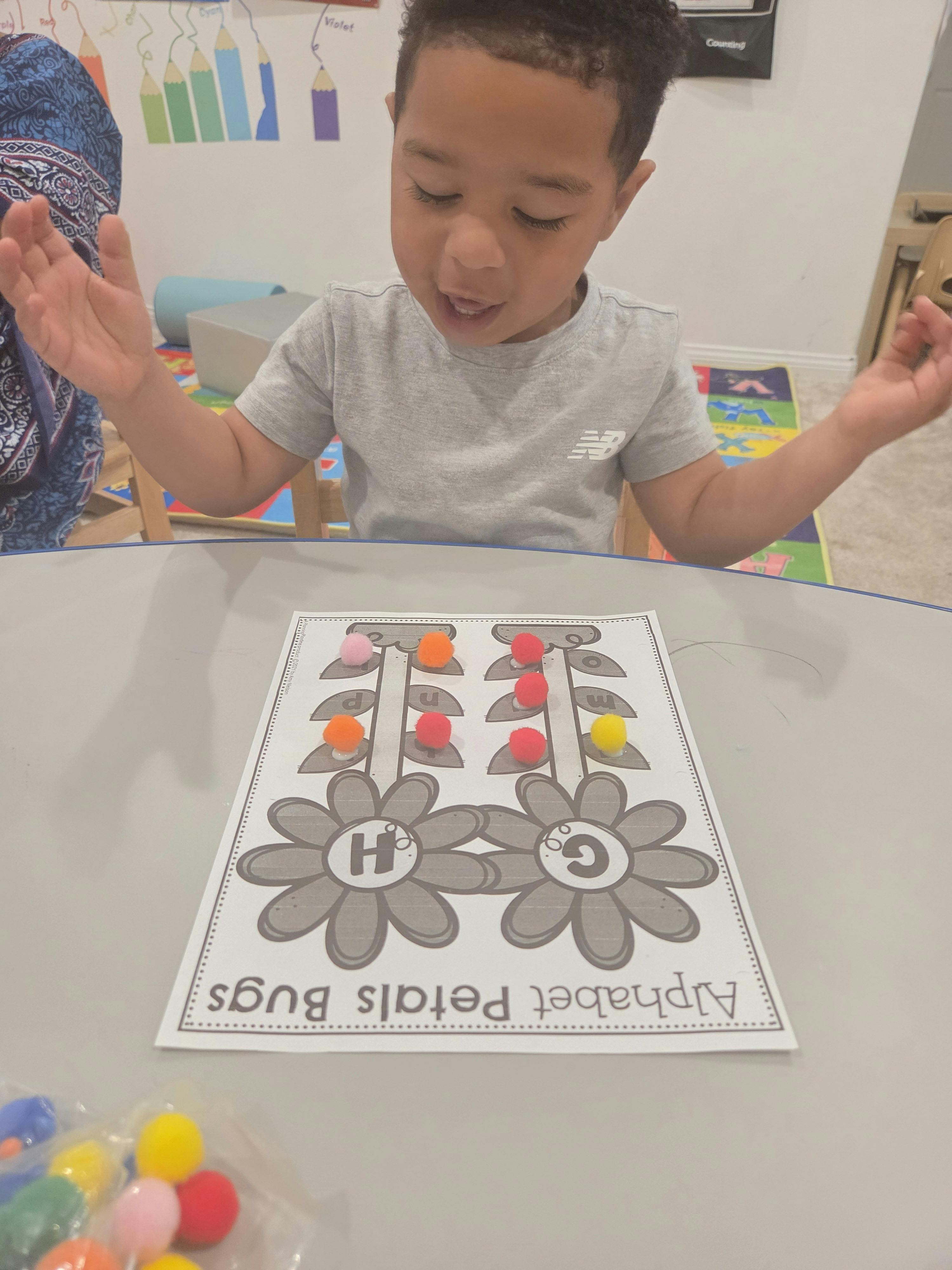 Child doing an alphabet activity with colorful pom-poms on a table