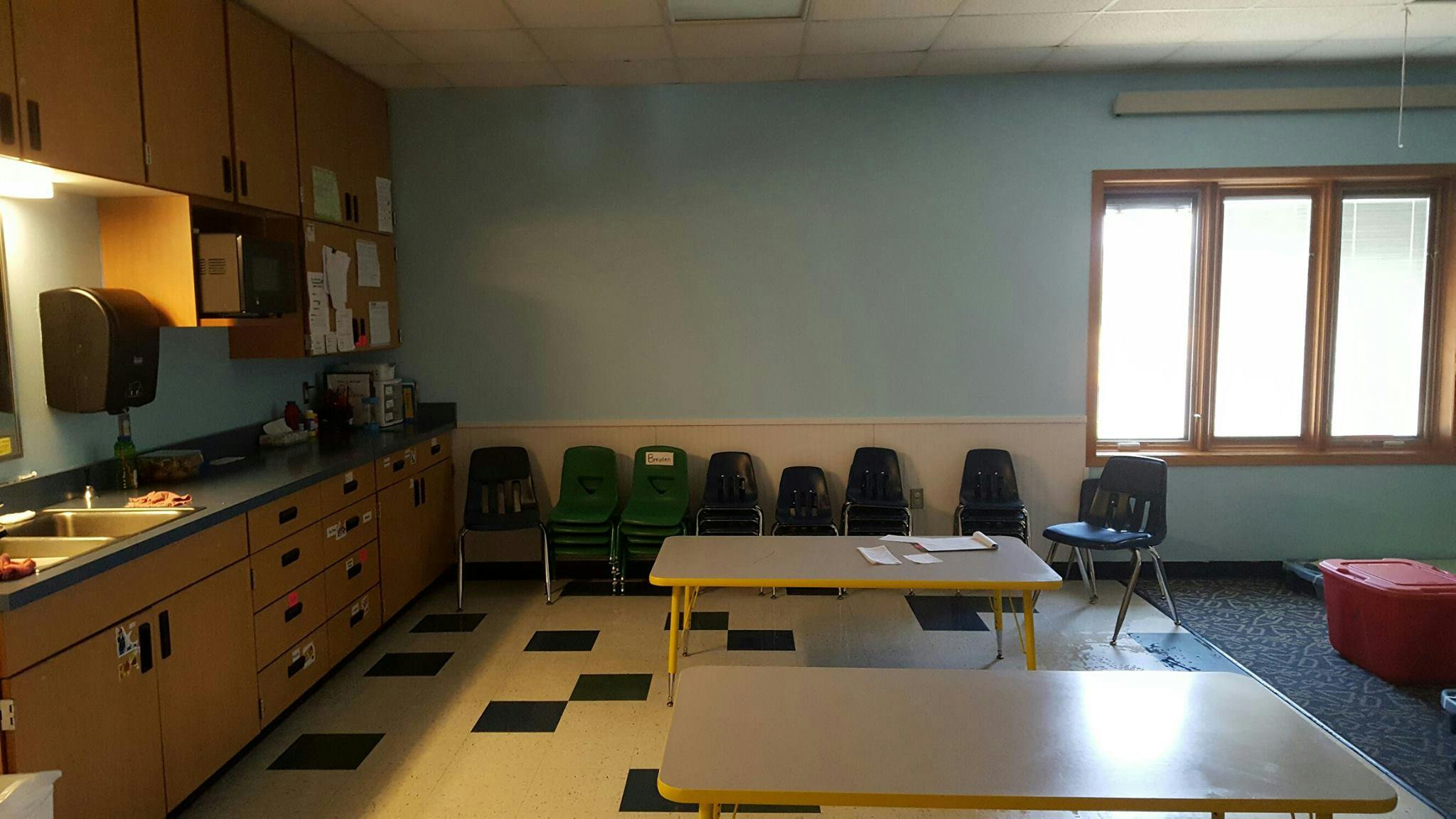Classroom with light blue walls, wooden cabinets, and small tables and chairs