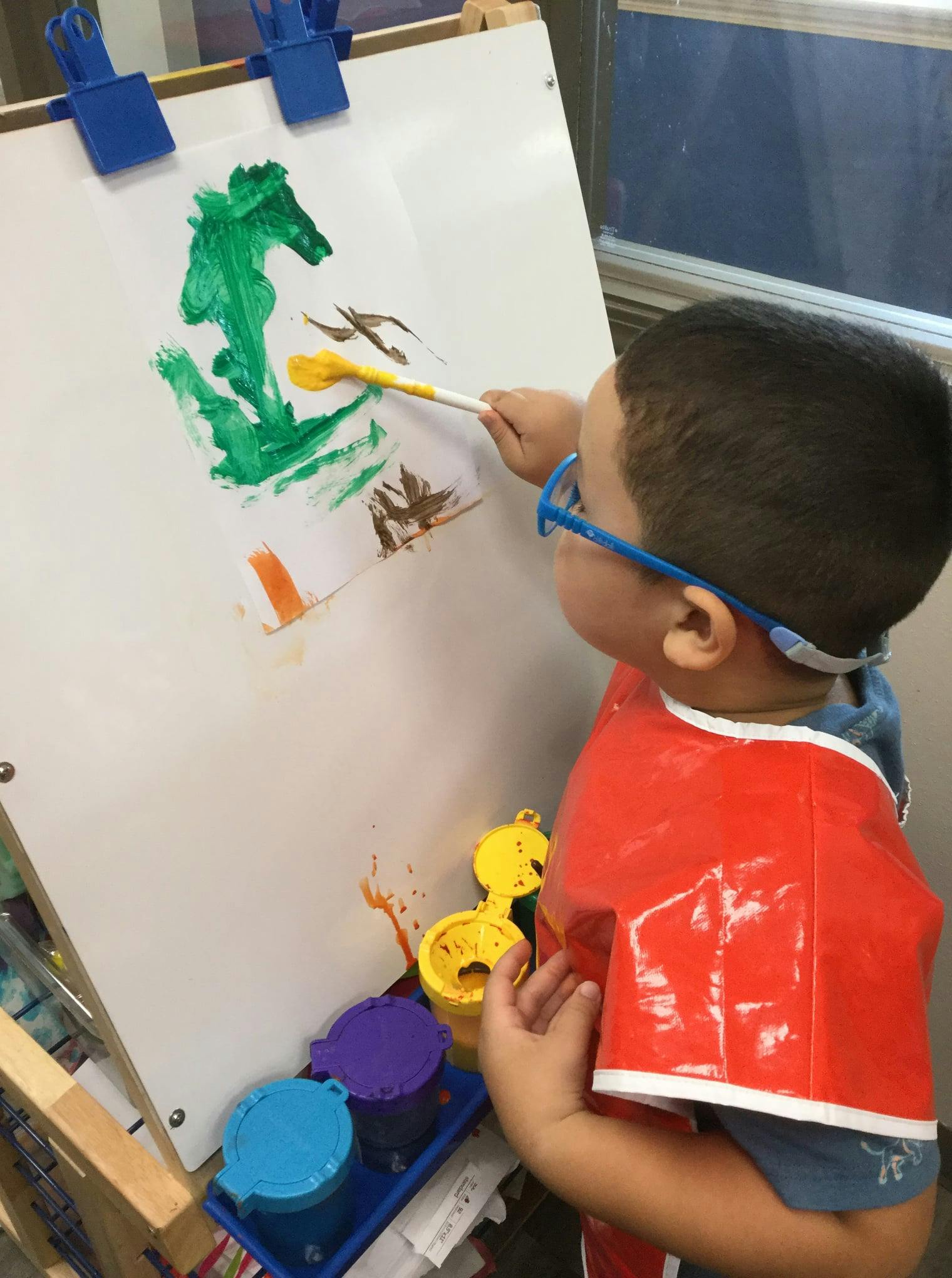 Child in an art smock painting on an easel