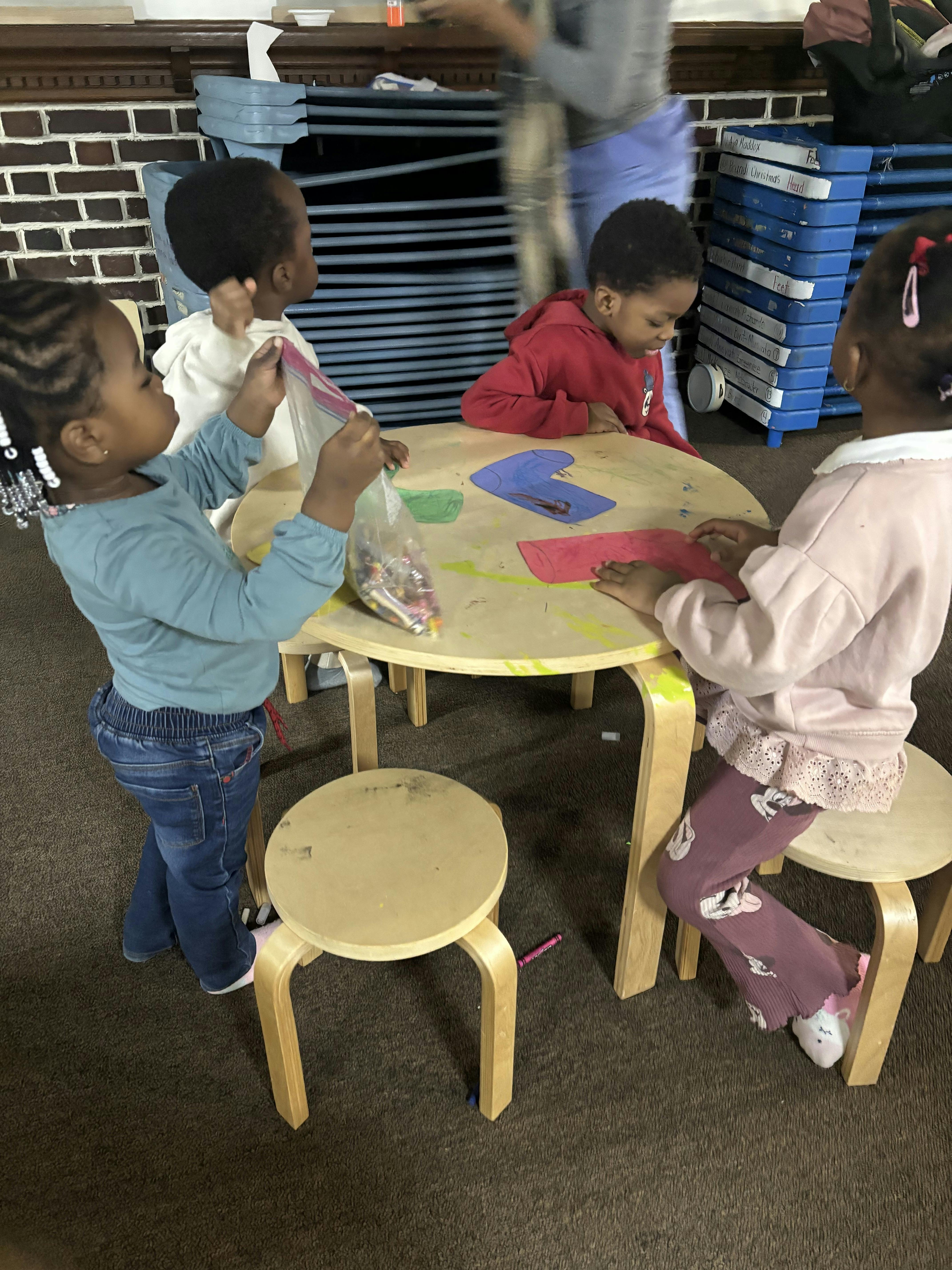 Four young children doing crafts at a small round table in a classroom