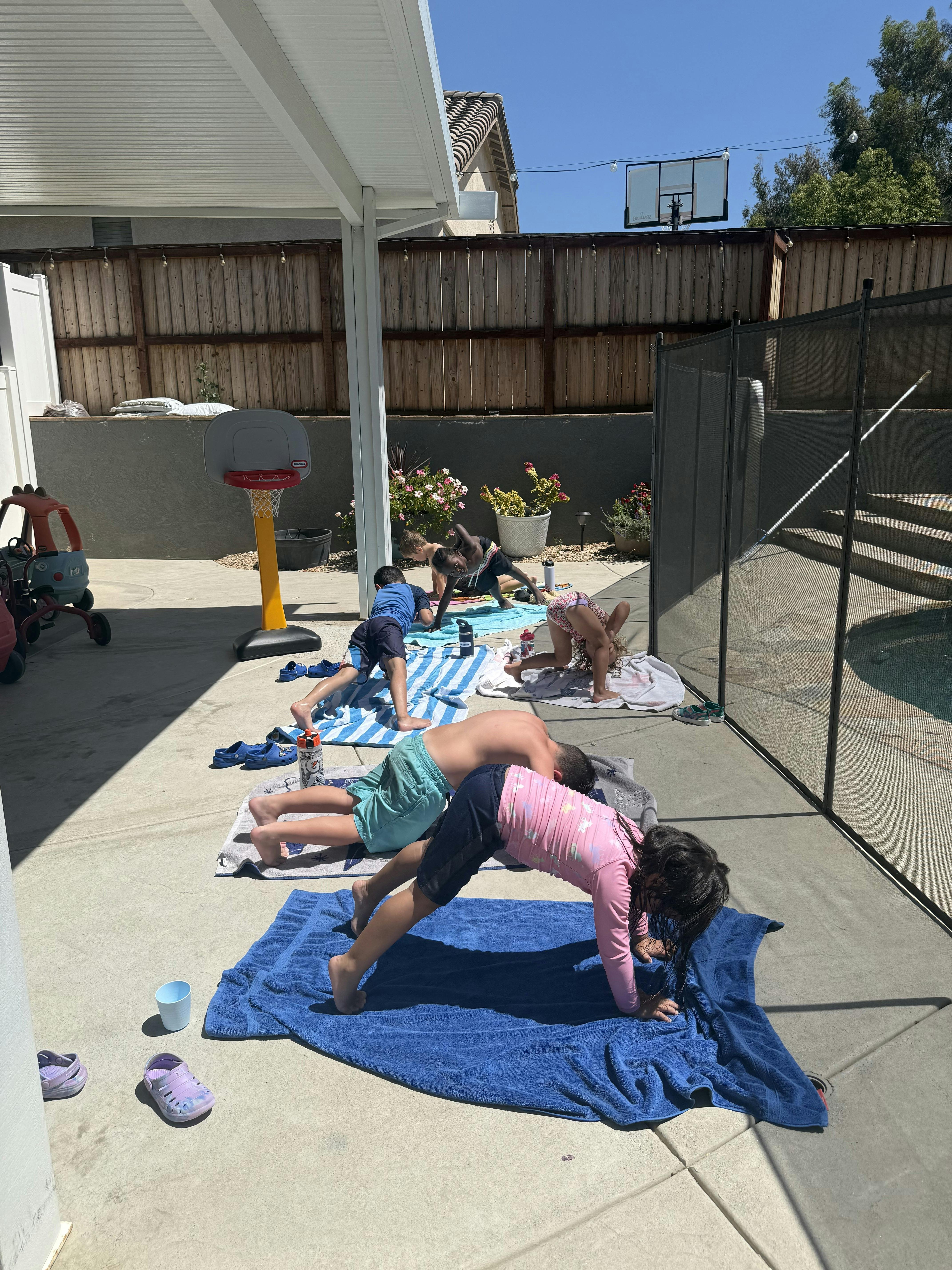 Group of children doing yoga poses on towels in a backyard