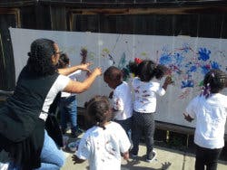 Adult and children painting on a large white canvas outdoors