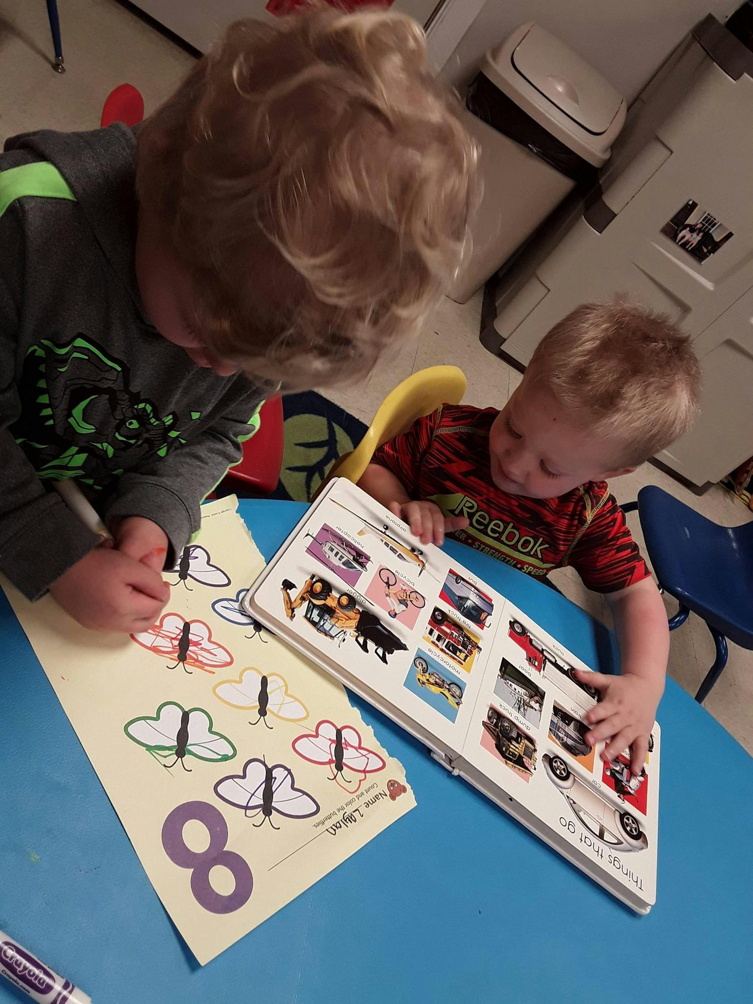 Two children at a table, one coloring butterflies, the other looking at a book