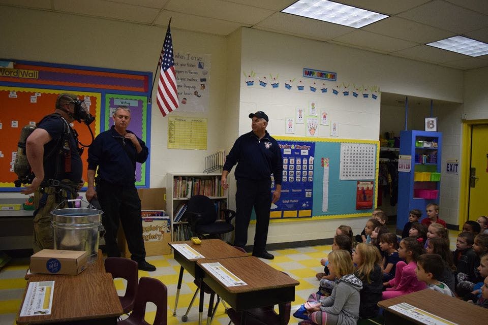 Three adults speaking to a group of children in a classroom