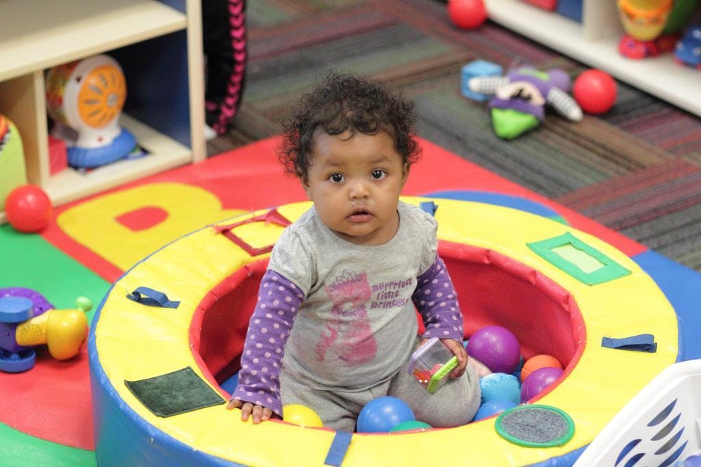 Child sitting in a colorful playpen with balls