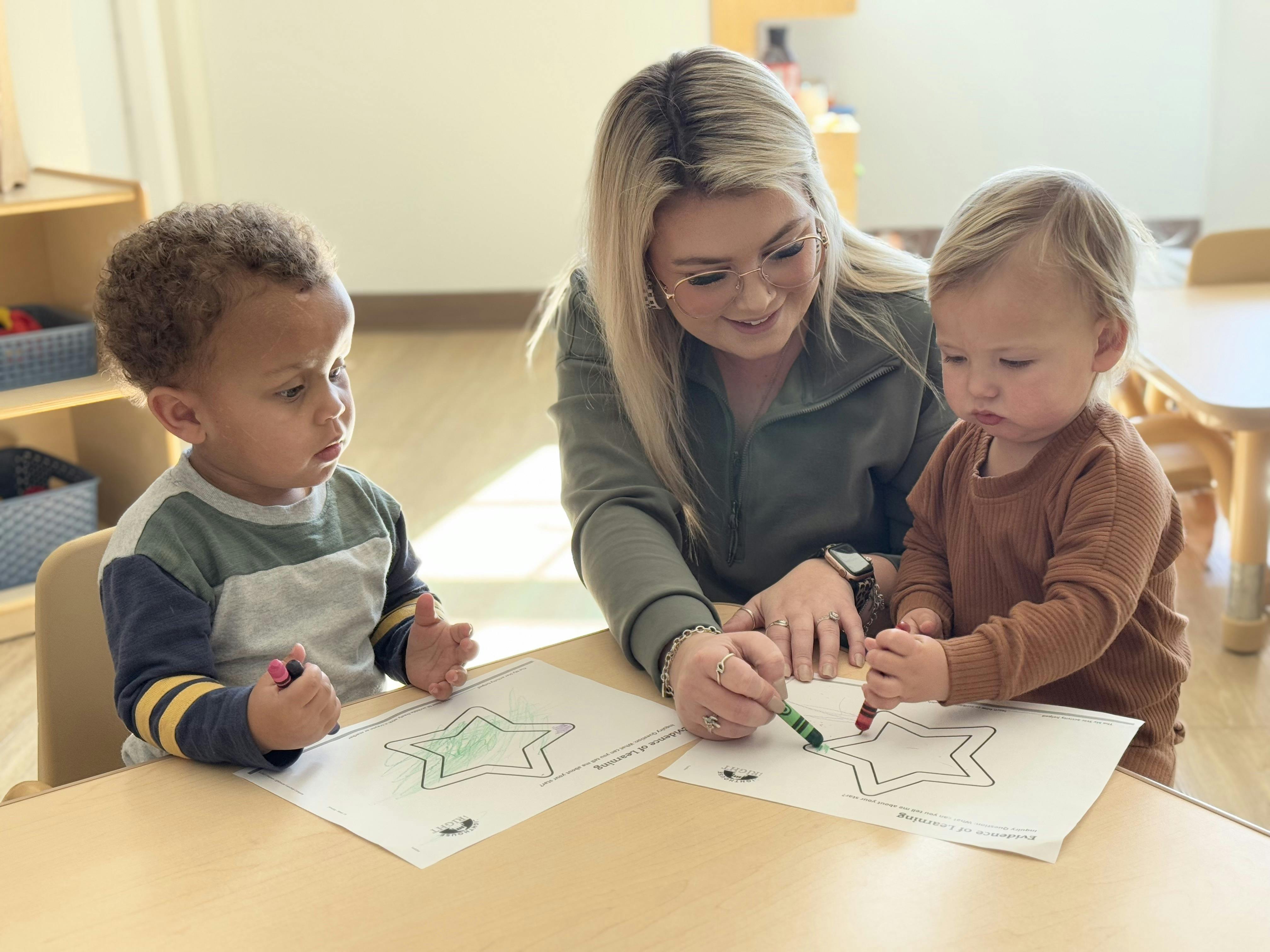 Adult assisting two children coloring star shapes at a table