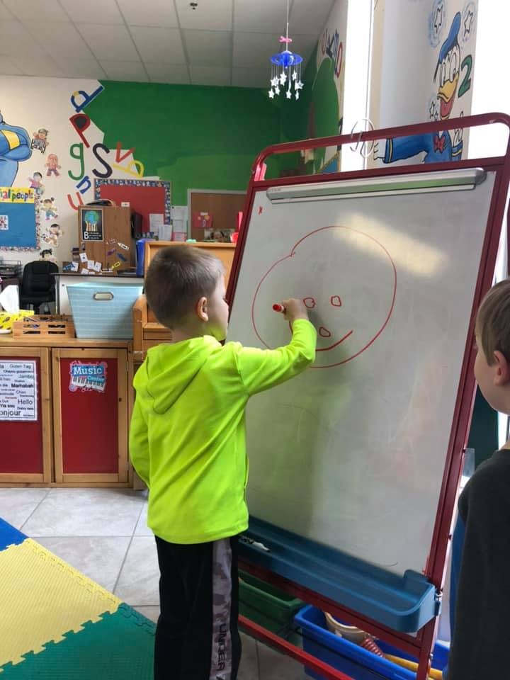 Child drawing a face on a whiteboard in a classroom