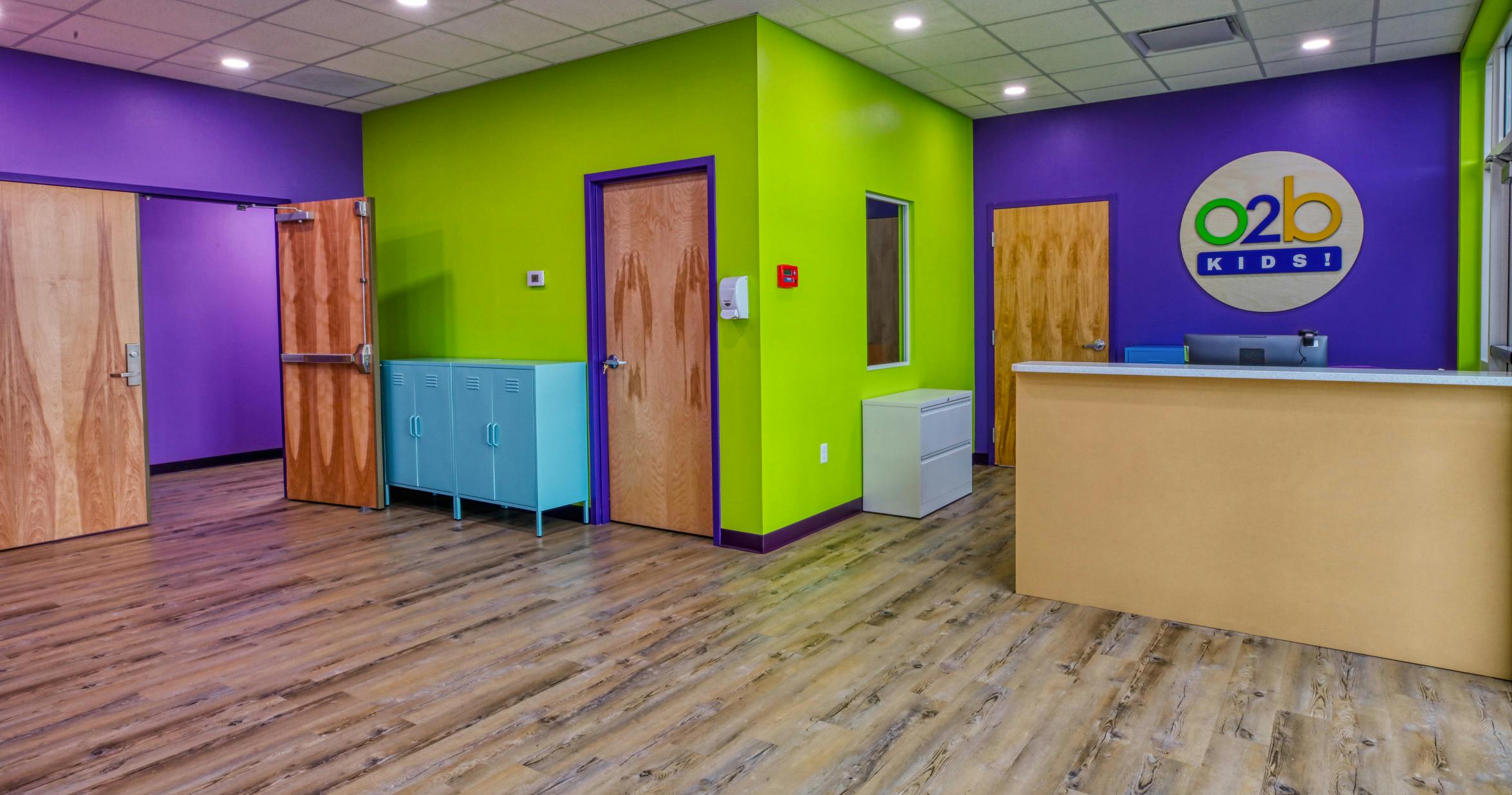 Lobby area with wood doors, blue lockers, and a reception desk, O2b Kids logo